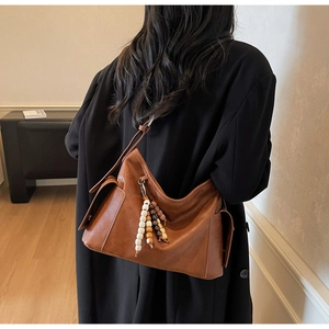 Detail view of large brown crossbody bag featuring retro wooden bead charms and side pockets