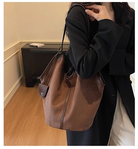 Detail of a large brown suede tote bag with leather trim worn on the shoulder of a model