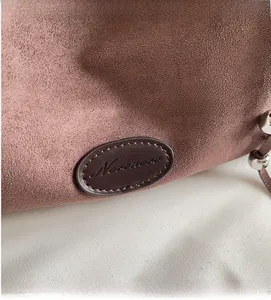 Detail einer braunen Wildleder-Tragetasche mit Leder-Logo-Patch und feinen Nähten