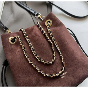 Détail du sac seau en cuir mat marron foncé avec chaîne dorée et logo embossé