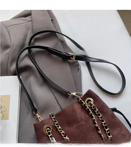 Détail d'un sac seau en daim marron avec une chaîne dorée et une bandoulière en cuir noir