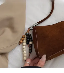 Détail d'un sac à bandoulière en daim marron avec breloque en perles et anneaux argentés