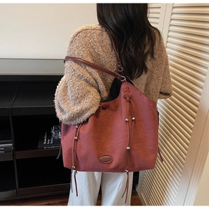 Detail of vintage burgundy suede tote bag with drawstring tassels worn by a model