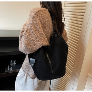 Detail of a black matte tote bag with side pendant shown on a brown sweater model