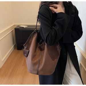 Detailed side view of large brown suede tote bag with leather piping on a female model