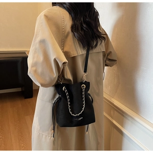 Vue détaillée d'un sac seau en faux daim noir avec chaîne dorée sur mannequin en trench