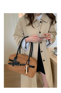 Brown suede crossbody bag with vintage beads charm and black handles on a beige coat model