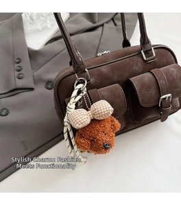Detail of cute brown teddy dog charm with plaid bow on a stylish leather tote bag