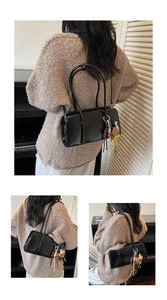Détail d'un sac sous les bras en cuir noir avec un pendentif ours et des accents de glands