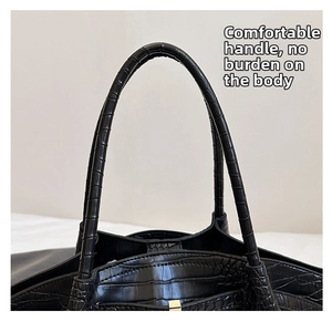 Detail of ergonomic round handle and fine stitching on black crocodile embossed handbag