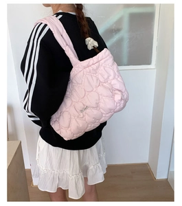 Detail of pink heart-quilted puffer tote bag with handmade metal logo and soft texture