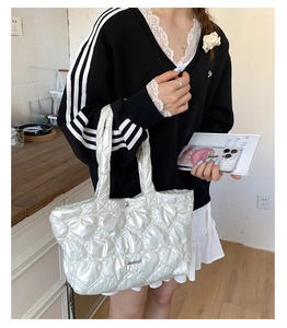 Detail of white quilted tote bag featuring heart patterns and polished metal logo plate