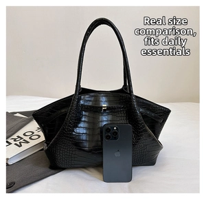 Black crocodile texture wing bag with silver buckle next to phone for size reference