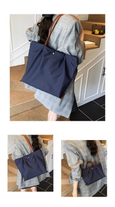 Detail van marineblauwe nylon draagtas met geplooid design en bruine leren handgrepen