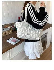 Detail of white quilted tote bag featuring glossy satin fabric and handmade metal logo