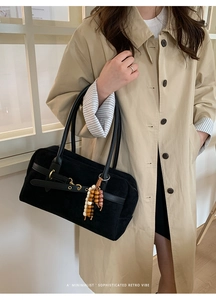Detail of black suede Boston bag with gold buckles and wooden bead charm on a beige coat