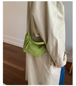 Detail of green suede underarm bag with silver chain strap on a model wearing a trench coat