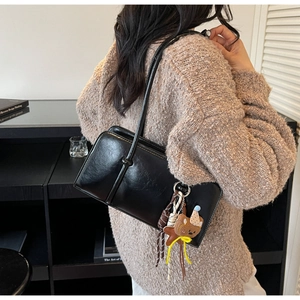 Détail du sac baguette en cuir noir avec un charm ours marron et des pompons colorés