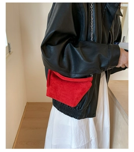 Detailed shot of a red suede underarm bag with silver chain strap worn by a model