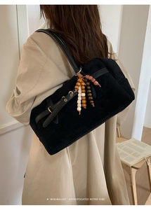 Detail of black suede shoulder bag featuring vintage wooden bead charm and minimalist strap