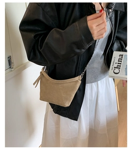 Detail of light khaki suede hobo bag with silver chain strap and fringe tassel on model