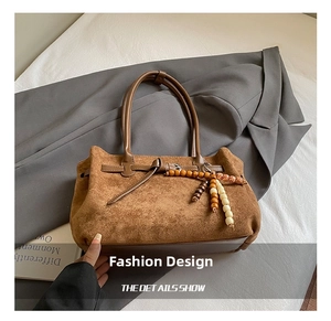 Dettaglio di una borsa tote in pelle scamosciata marrone con ciondolo in legno e fibbia