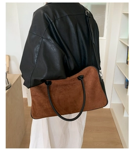 Detail of a large brown suede tote bag with black leather straps on a model's shoulder