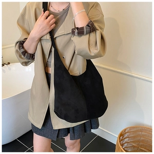 Détail d'un grand sac bandoulière en daim noir porté par un mannequin dans un décor intérieur