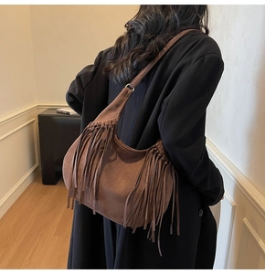 Close-up of brown suede hobo bag with fringe details worn by a model in soft light