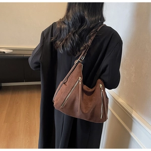 Detail of dark brown suede hobo bag with vertical zippers styled on a black wool coat