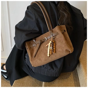 Close-up of brown suede tote bag with leather buckle detail and wooden bead charm