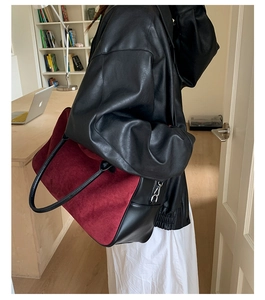 Close-up of burgundy suede tote with black leather trim and silver zipper detail