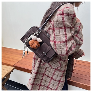 Detail of dark brown vintage suede shoulder bag with plush bear charm on model