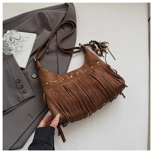 Détail du sac seau en daim marron avec rivets en étoile et franges sur un blazer gris