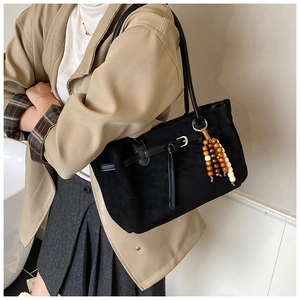 Detail of black matte tote bag featuring colorful wooden bead charm and leather handles