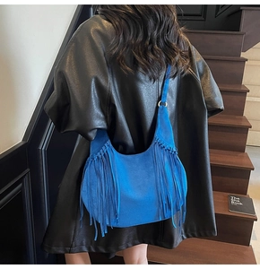 Detail of vibrant blue suede crescent bag with long fringes worn on the shoulder