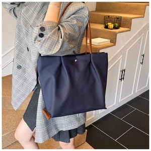 Detailaanzicht van grote marineblauwe nylon tote bag met plooiontwerp en bruine leren riemen