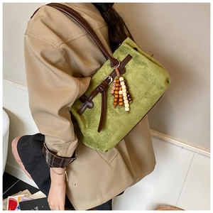 Dettaglio borsa tote in pelle scamosciata verde con manici marroni e nappe in legno
