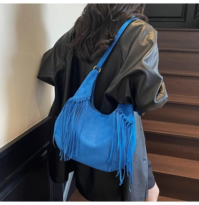 Blue suede hobo bag with fringe details worn by a model in a retro style outfit