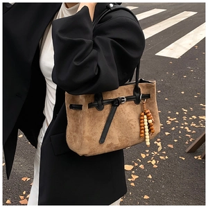 Detail of vintage brown suede tote bag with wooden bead pendant on city street