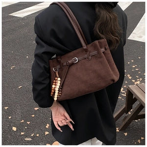 Detail of dark brown matte tote bag with leather buckle and wooden bead tassel ornament