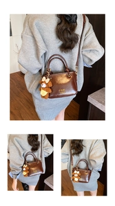 Détail d'un sac seau marron avec lettres dorées, breloque ours et double bandoulière