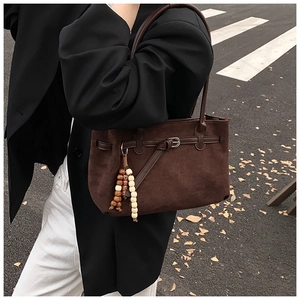 Dettaglio della borsa tote in pelle scamosciata marrone scuro con ciondolo e fibbie in metallo