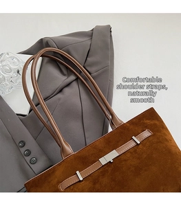 Brown suede bucket bag detail with leather strap and silver metal buckle on grey suit