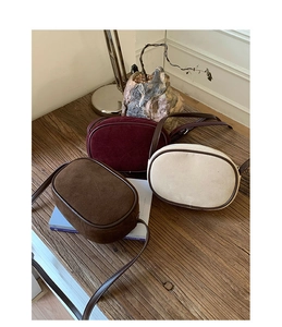 Three oval suede crossbody bags in brown wine red and beige on a wooden surface
