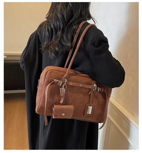 Close-up of brown suede hobo bag with buckled straps and a mini charm on a model