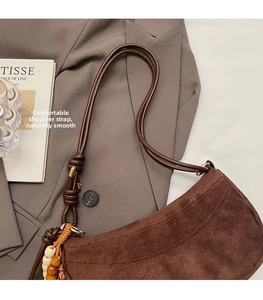 Detail of dark brown suede shoulder bag featuring a unique knot strap and wooden bead charm