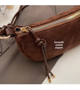 Detailed close-up of the smooth golden zipper and brown suede texture on this croissant bag