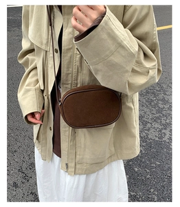 Close-up of a dark brown suede crossbody bag with minimalist oval design and sleek piping