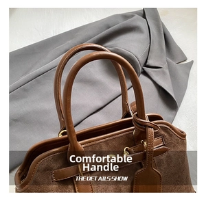 Detail of suede handbag showing leather handles and gold metal hardware accents